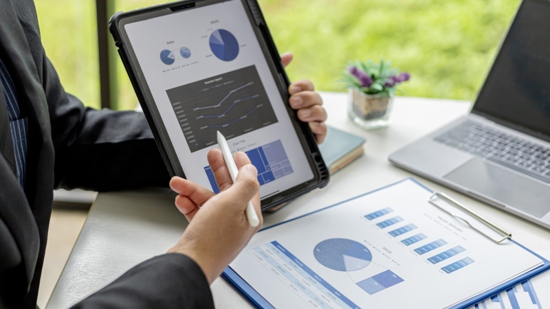 Business professional reviewing sales dashboard and performance analytics on tablet and reports.