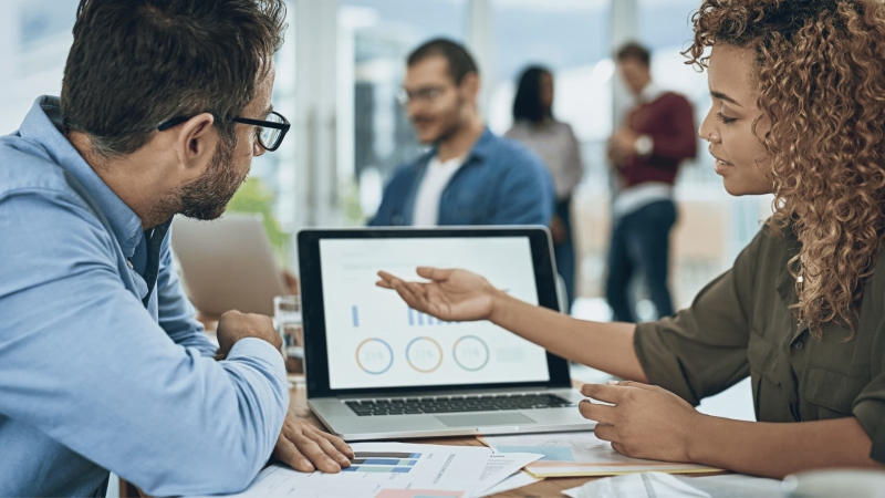 Business professionals analyzing charts and graphs on a laptop during a meeting in a modern office