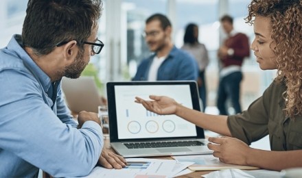 Business professionals analyzing charts and graphs on a laptop during a meeting in a modern office