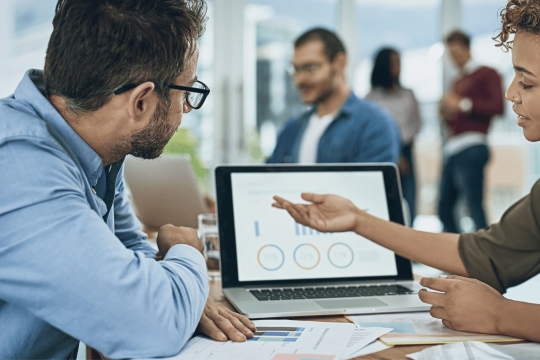 Business professionals analyzing charts and graphs on a laptop during a meeting in a modern office